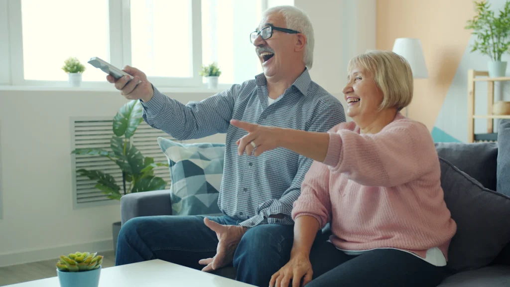 Un couple de retraités souriants utilise la télécommande de leur téléviseur