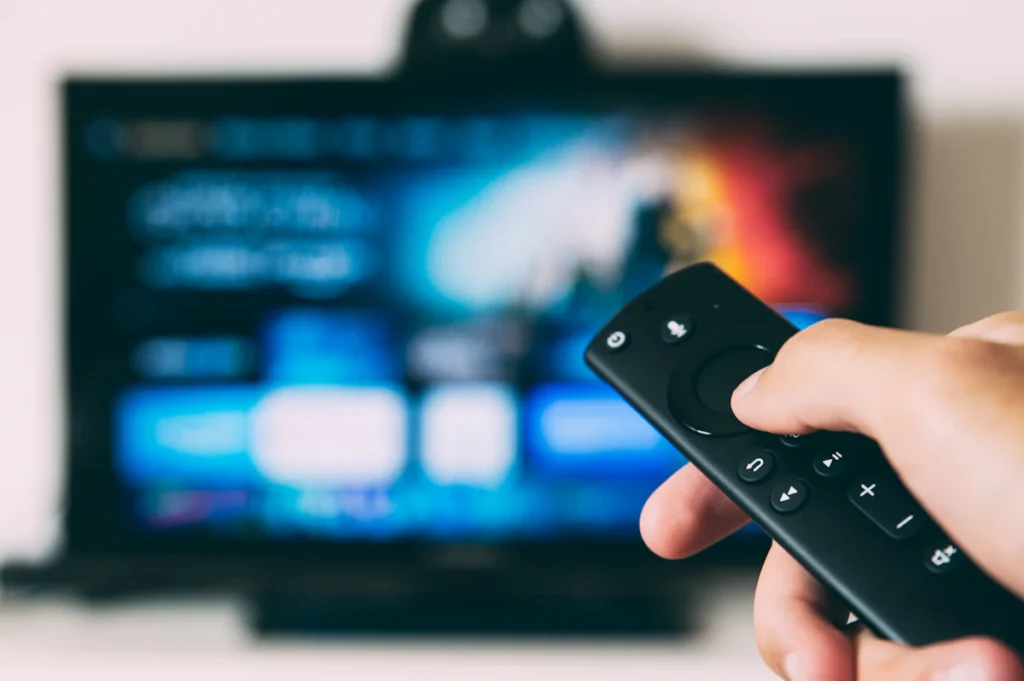 Une main tient une télécommande devant le menu d’un téléviseur intelligent